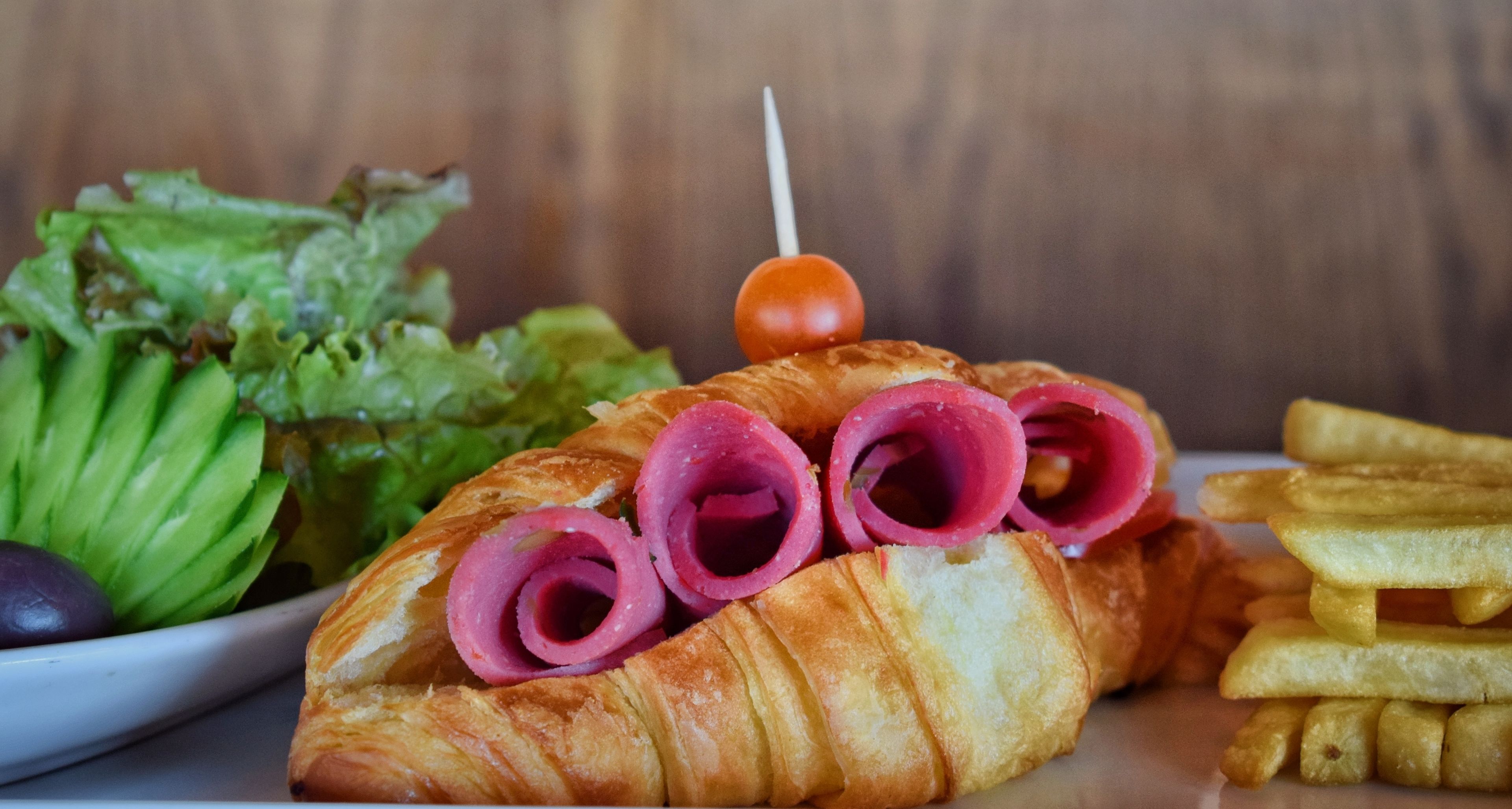A croissant with ham and a cherry on top, accompanied by a side of fries and a salad.