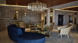 A modern lobby with a blue sectional sofa, a round coffee table, and a beige armchair. - Romance Alexandria Hotel (Alexandria)