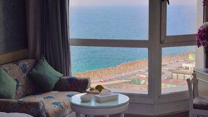 A hotel room with a bed, a sofa, a small table, and a view of the beach and ocean. - Romance Alexandria Hotel (Alexandria)