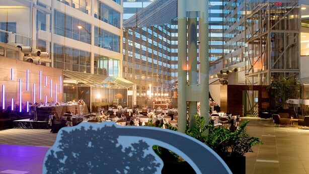 A modern hotel atrium with multiple floors, glass railings, and a central decorative tree sculpture.
