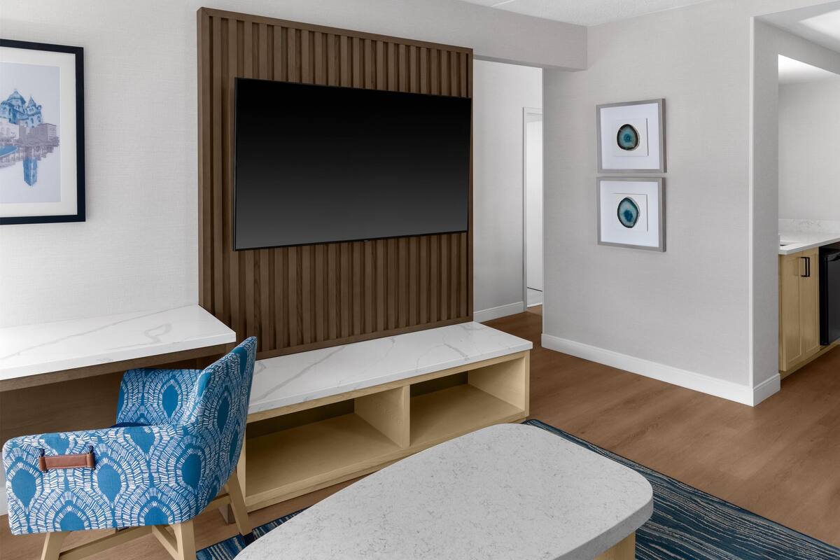 Ein modernes Wohnzimmer mit Fernseher, einer Bank, einem blauen Stuhl mit Muster und zwei gerahmten Bildern an der Wand.