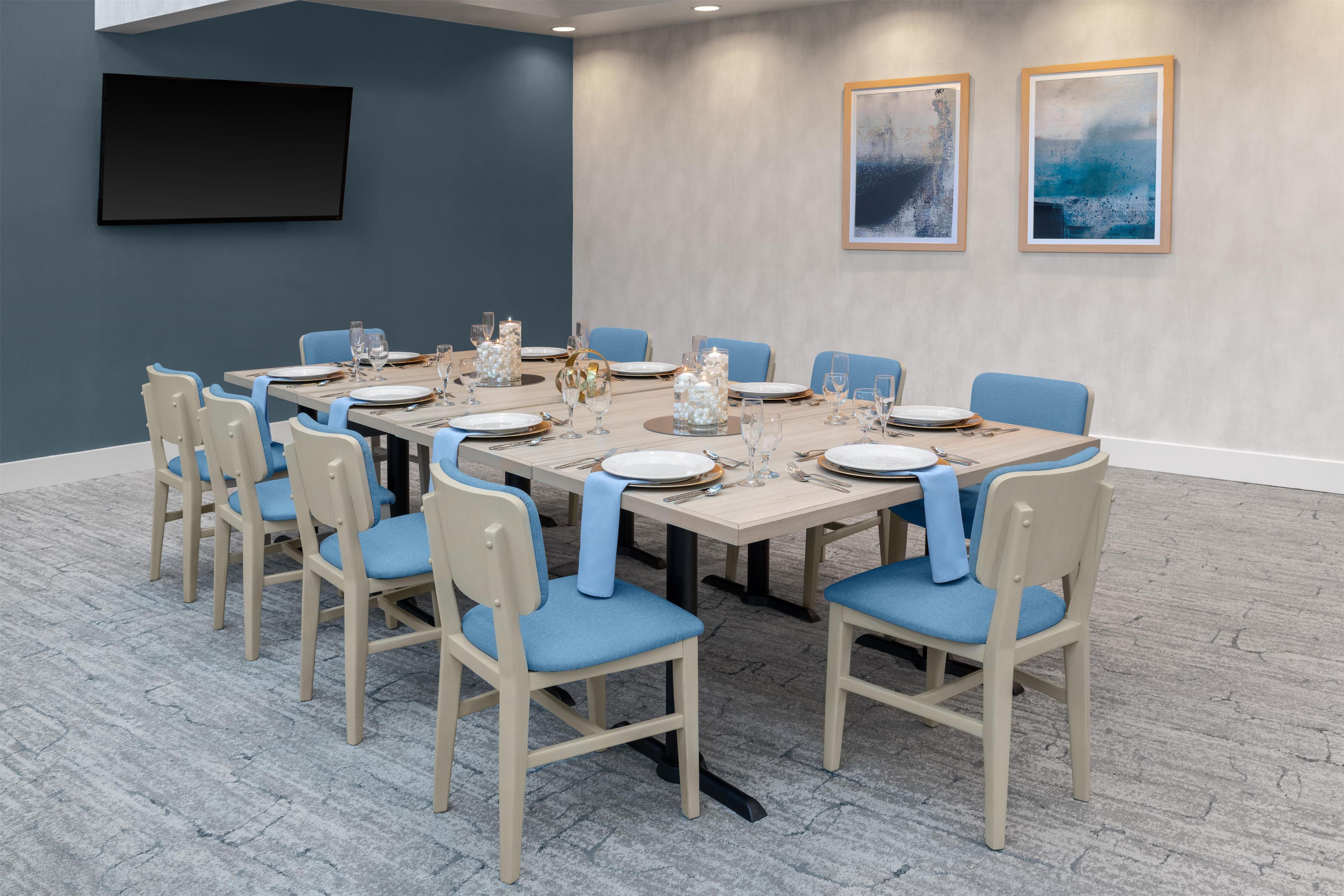 A conference room with a long table set for a meeting, surrounded by chairs with blue cushions.