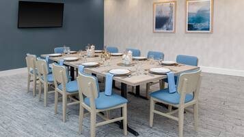 A conference room with a long table set for a meeting, surrounded by chairs with blue cushions.