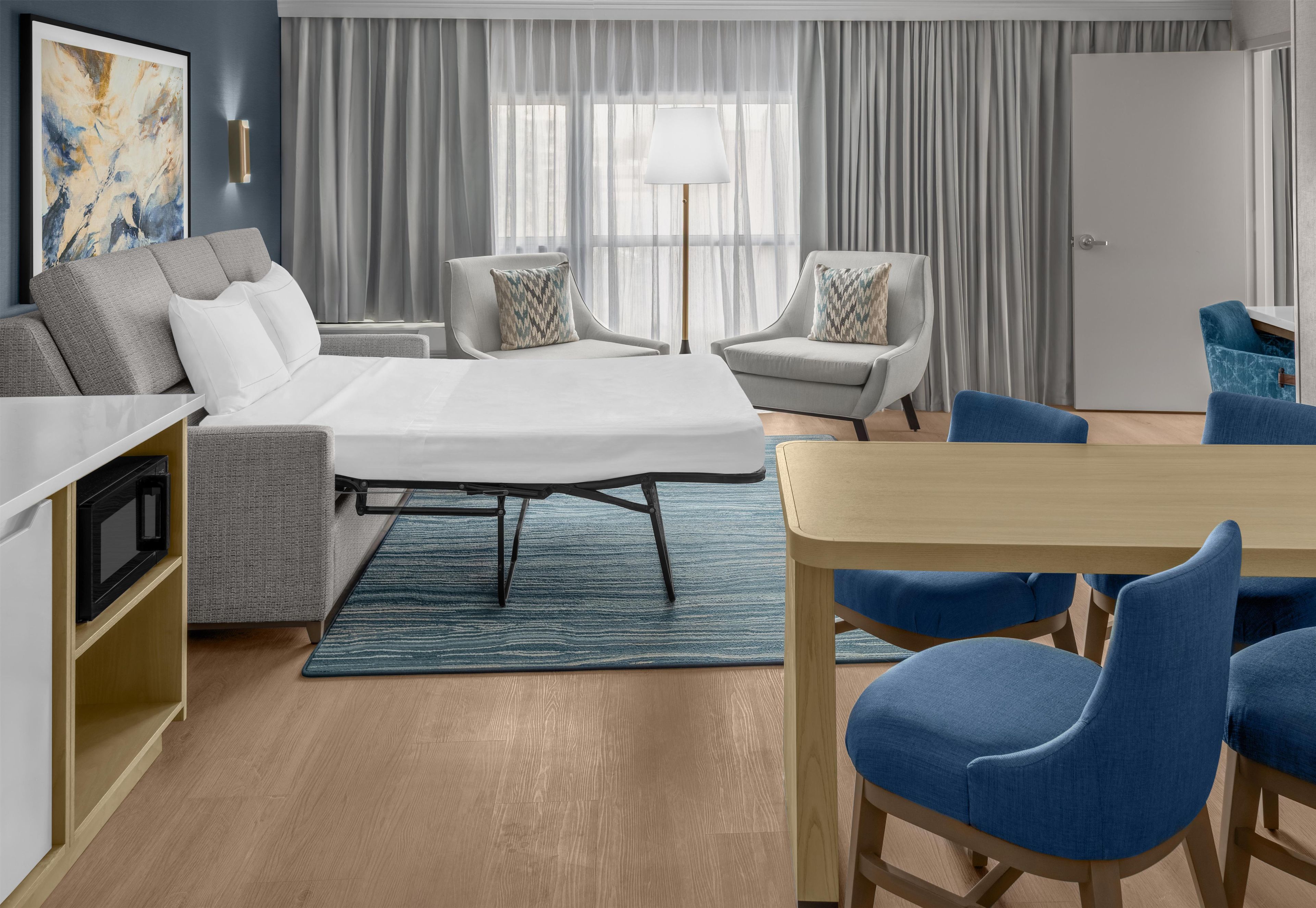 Una habitación de hotel moderna con cama, sofá, sillas, una mesa de comedor y vistas a la ciudad.