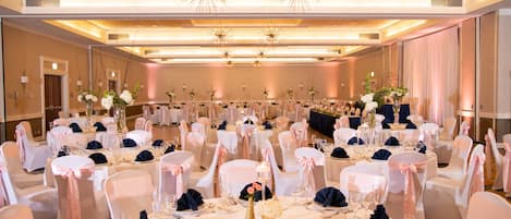Une salle de banquet avec des tables rondes, des chaises blanches et bleu marine, et des centres de table floraux.