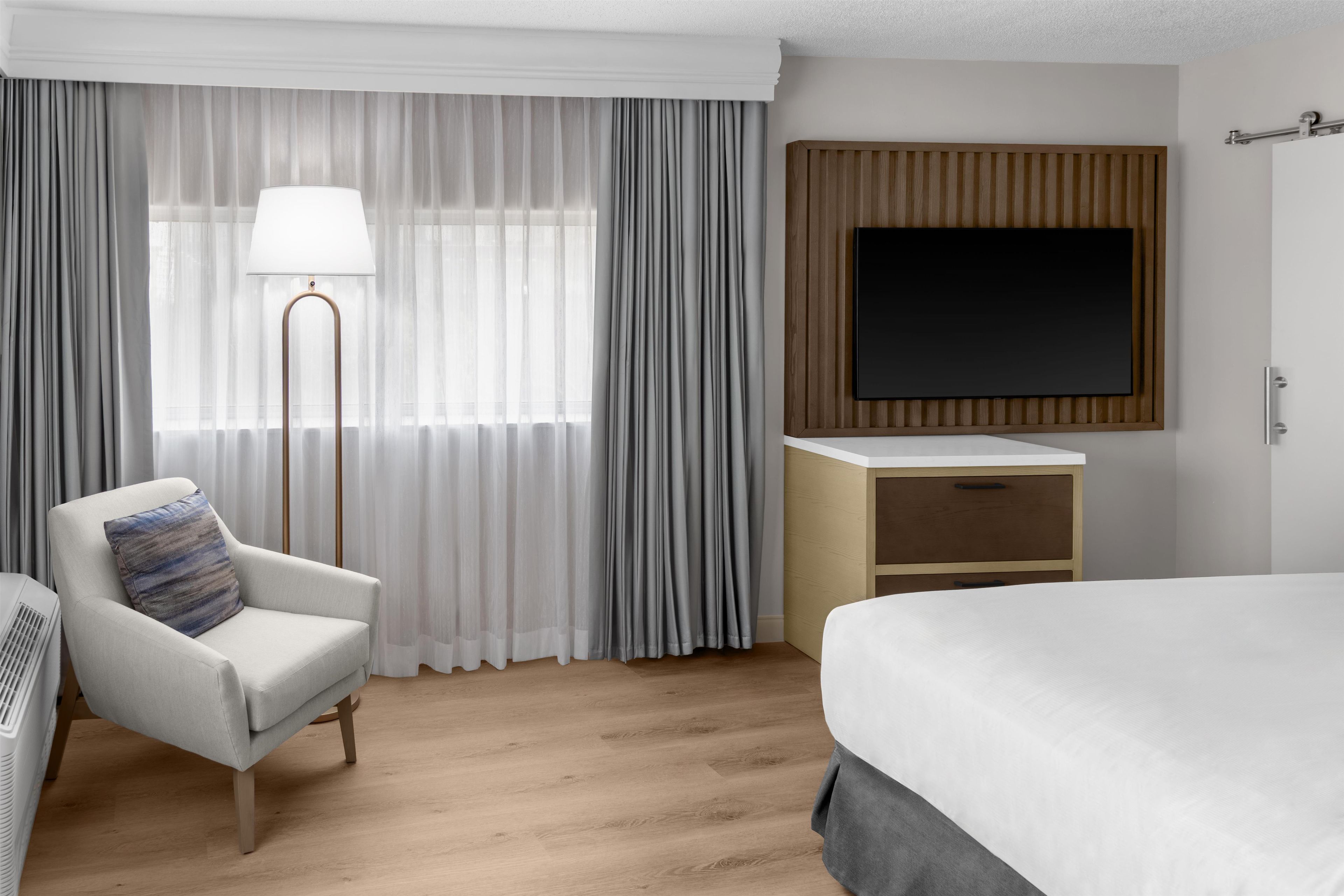 Een hotelkamer met een bed, een bureau, een stoel, een televisie en een raam met gordijnen.