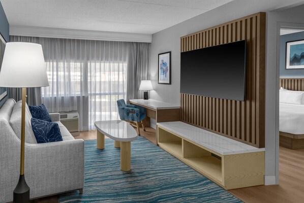 A modern hotel room with a sofa, a desk, a TV, and a bed.