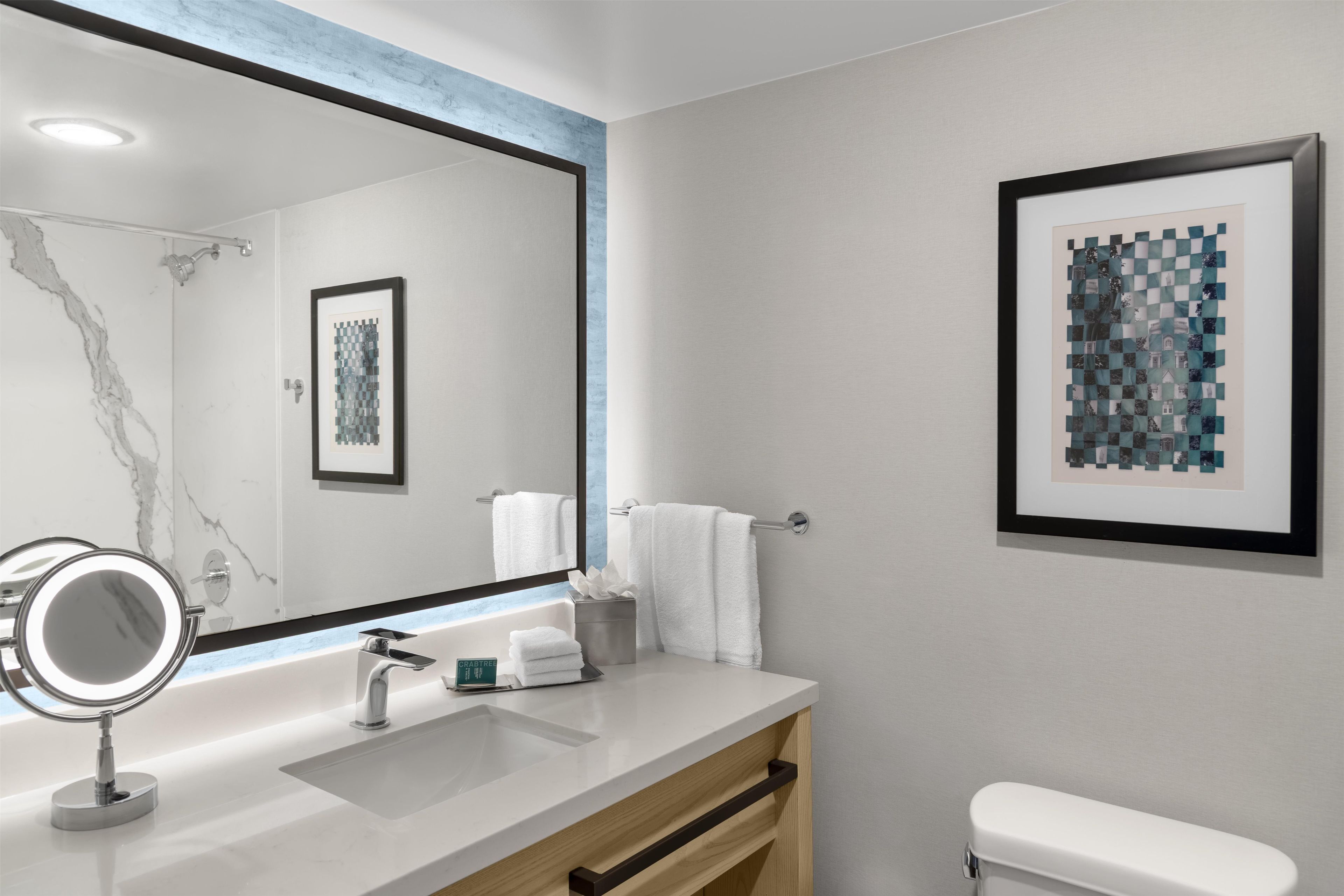 Een moderne badkamer met een grote spiegel, een wastafel, een toilet en een kunstwerk in een lijst aan de muur.