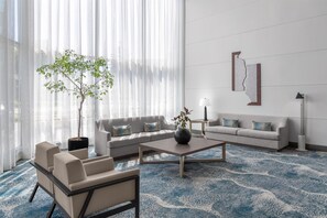 A modern living room with a sofa, armchairs, a coffee table, a potted plant, and a large window with sheer curtains.