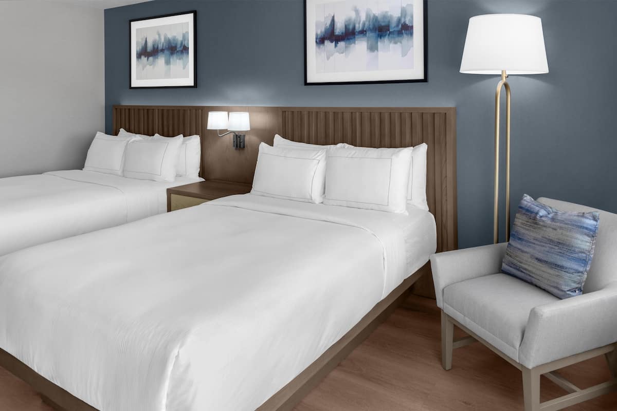 Ein Hotelzimmer mit zwei Betten, einem Nachttisch mit Lampe, einem Sessel und zwei Wandleuchten.
