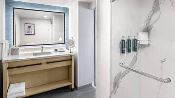 A modern bathroom with a large mirror, wooden vanity, and a marble shower area.