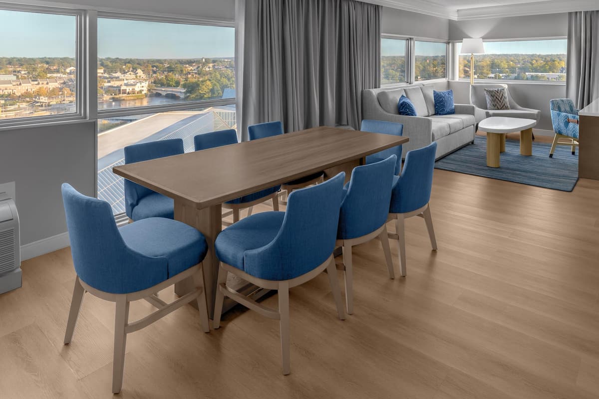 Ein modernes Hotelzimmer mit Essbereich, einer Sofagarnitur und Blick auf die Stadt.