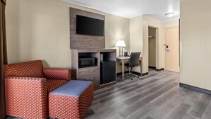 A hotel room with a sofa, a desk, a TV, a lamp, and a refrigerator. - Travelodge by Wyndham Rapid City (Rapid City)
