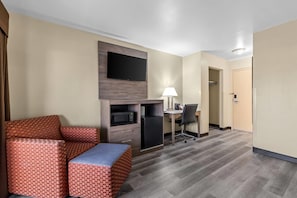 Habitación de hotel con sofá, escritorio, televisión de pantalla plana, refrigerador, lámpara y puerta.