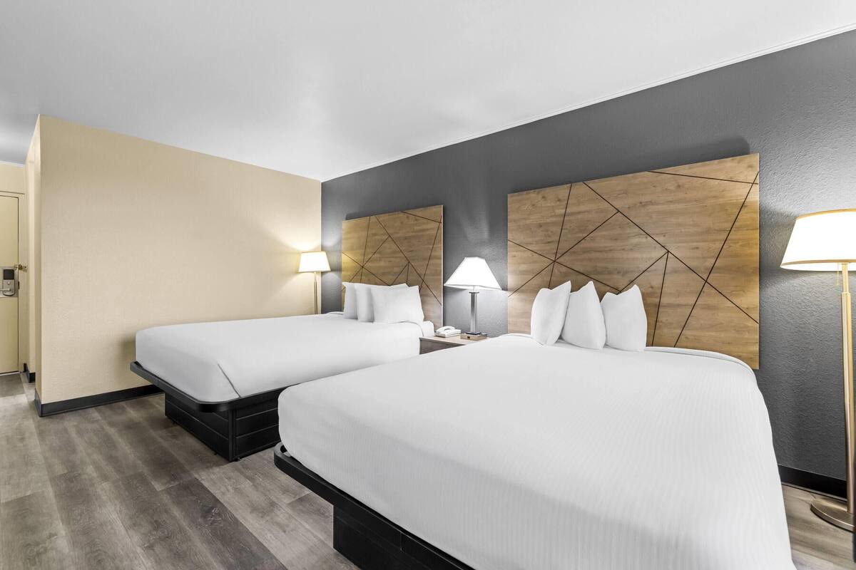 Ein Hotelzimmer mit zwei Betten, einer Wand mit Holzvertäfelung und einem Nachttisch mit Lampe.
