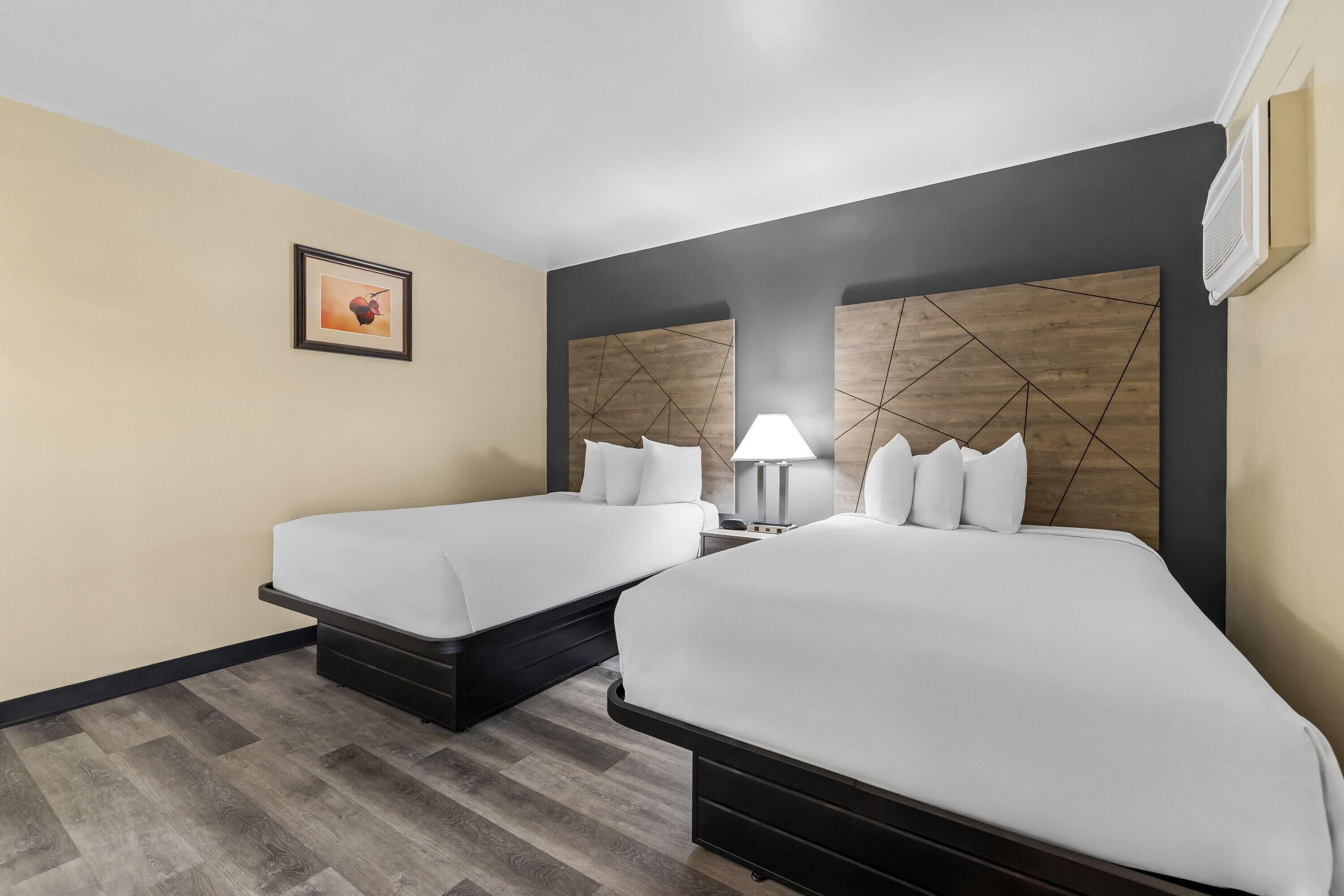 Habitación de hotel con dos camas, una mesita de noche, una lámpara y un cuadro en la pared.