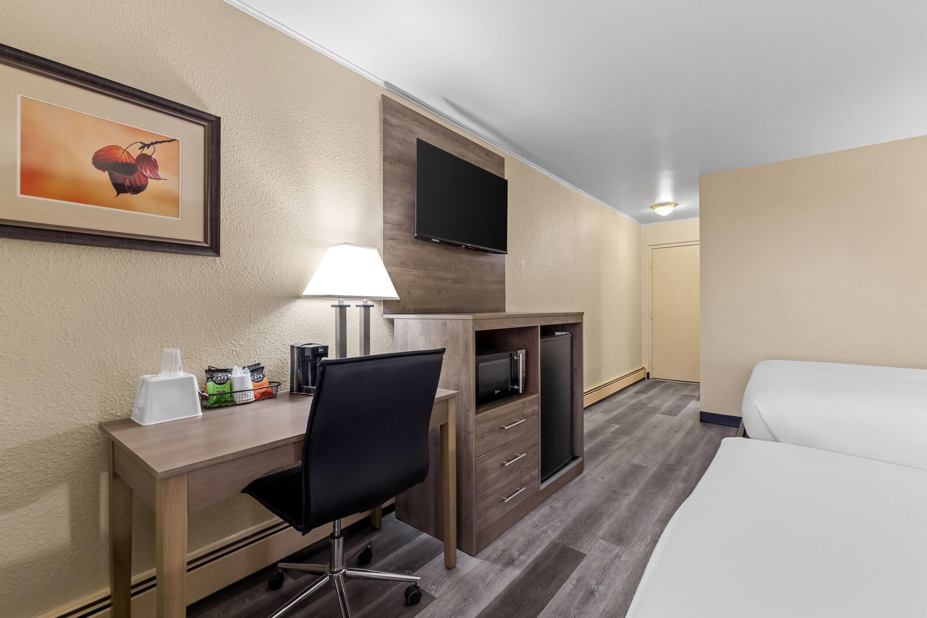 A hotel room with a desk, chair, TV, bed, and a framed picture on the wall.