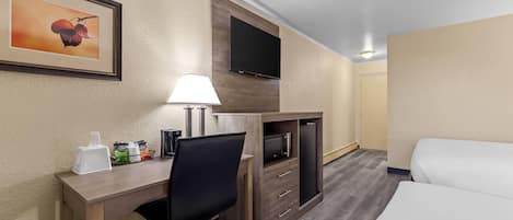 A hotel room with a desk, chair, TV, bed, and a framed picture on the wall.