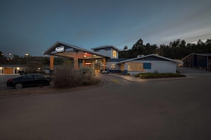 A Travelodge hotel with a covered entrance, a car parked in front, and a building with a flat roof. - Travelodge by Wyndham Rapid City (Rapid City)