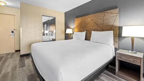 A hotel room with a large bed, bedside tables, a mirror, and a modern headboard. - Travelodge by Wyndham Rapid City (Rapid City)