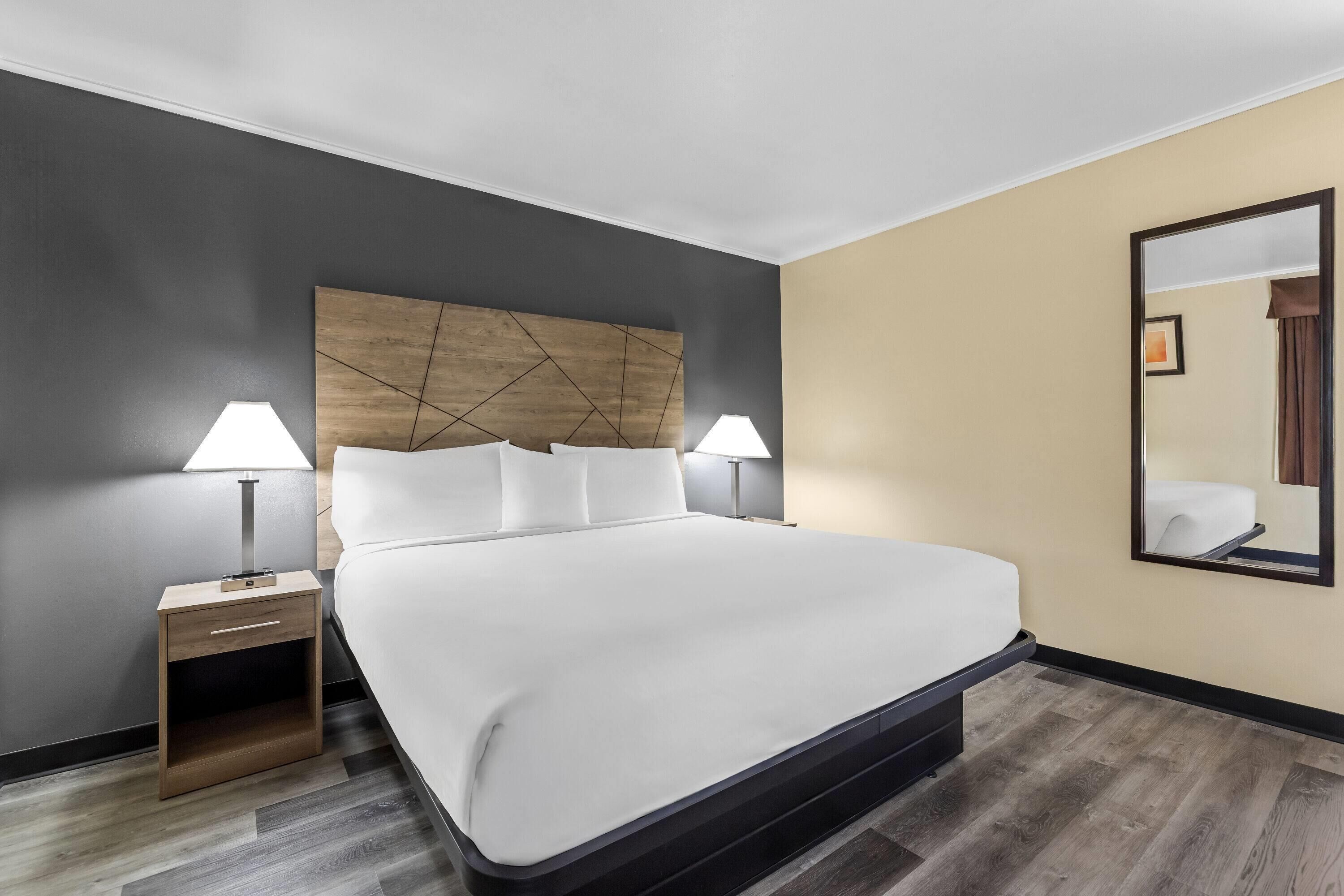 A hotel room with a large bed, two bedside tables with lamps, a wooden headboard, and a large mirror on the wall.