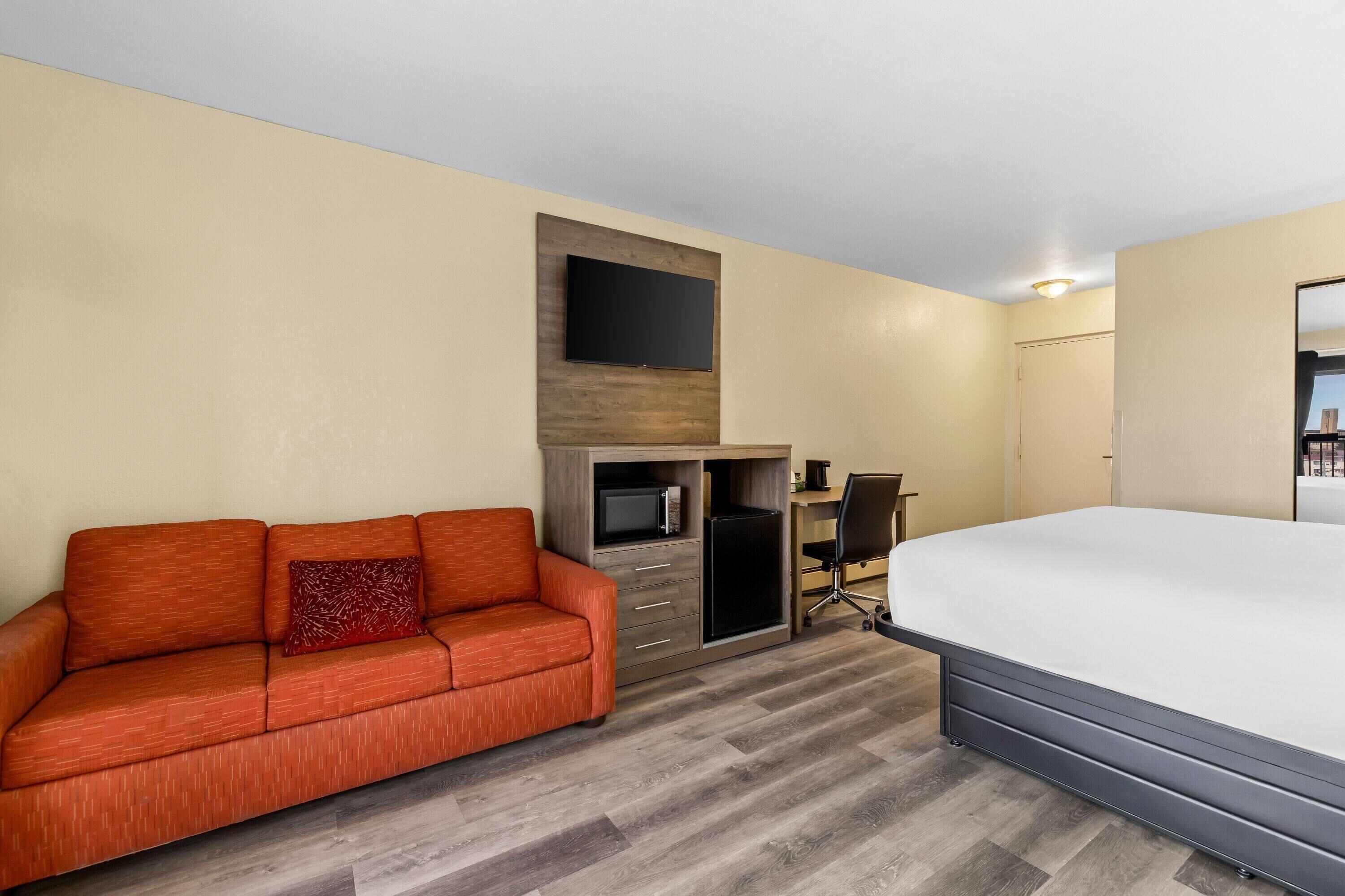 Habitación de hotel con cama, sofá, escritorio con silla, televisor montado en la pared y microondas.