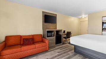 Habitación de hotel con cama, sofá, escritorio con silla, televisor montado en la pared y microondas.