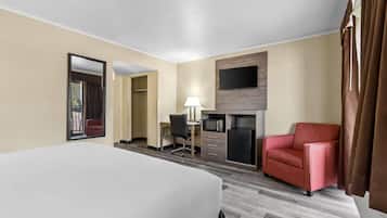 A hotel room with a bed, a desk with a chair, a TV mounted on the wall, and a red armchair.