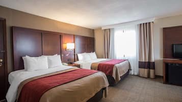 A hotel room with two beds, a TV, and a desk.