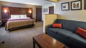 A hotel room with a bed, a sofa, a coffee table, and framed pictures on the wall.