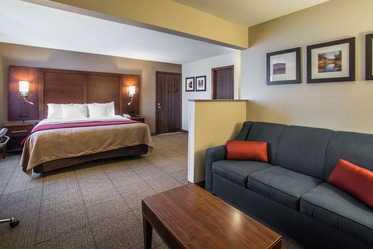 A hotel room with a bed, a sofa, a coffee table, and framed pictures on the wall.
