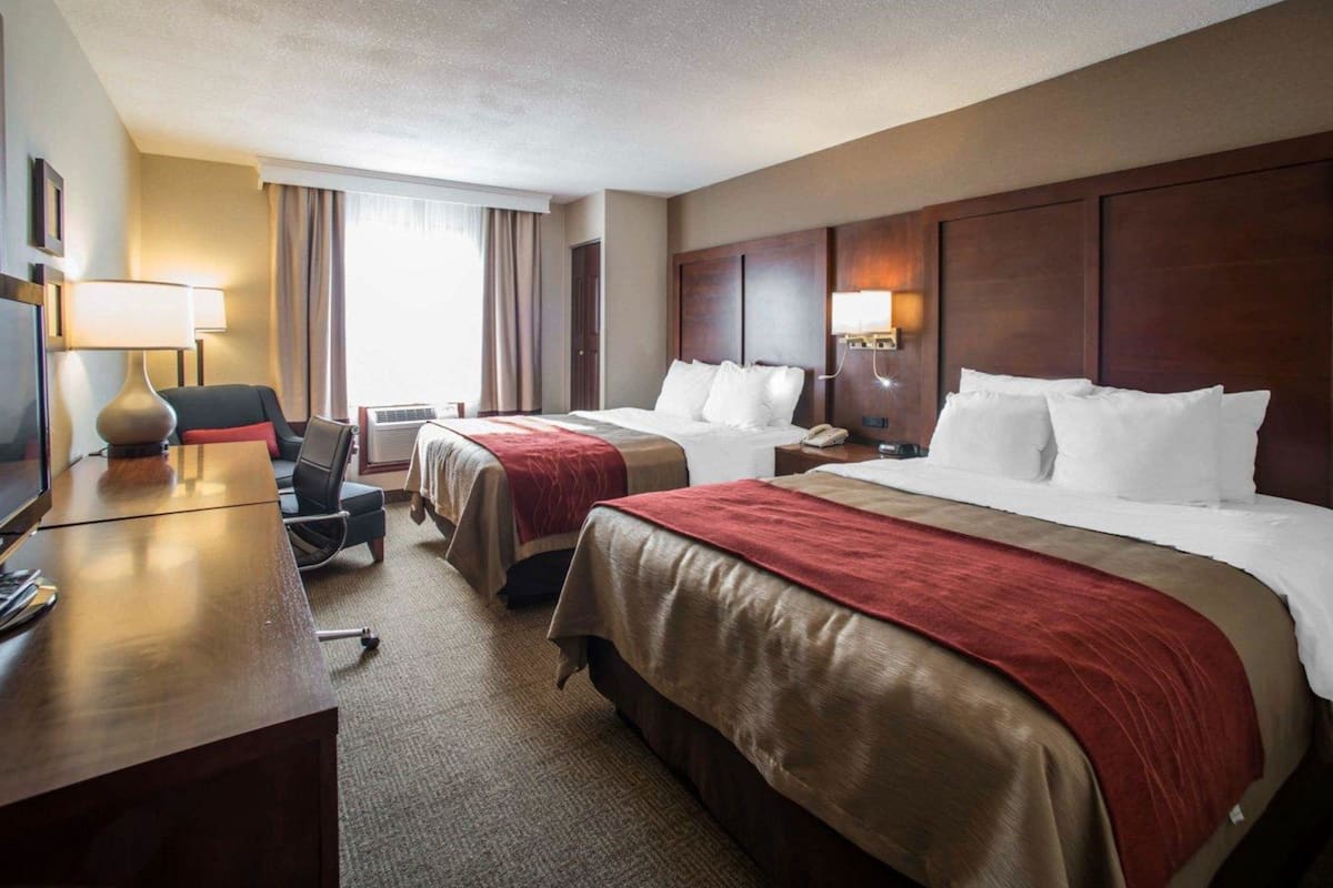 A hotel room with two beds, a desk with a lamp, a chair, and a television.