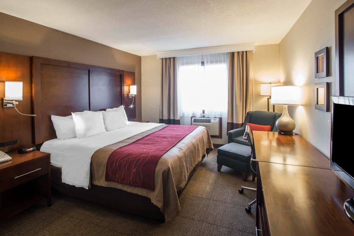 A hotel room with a large bed, a desk with a chair, a TV, and a window with curtains.