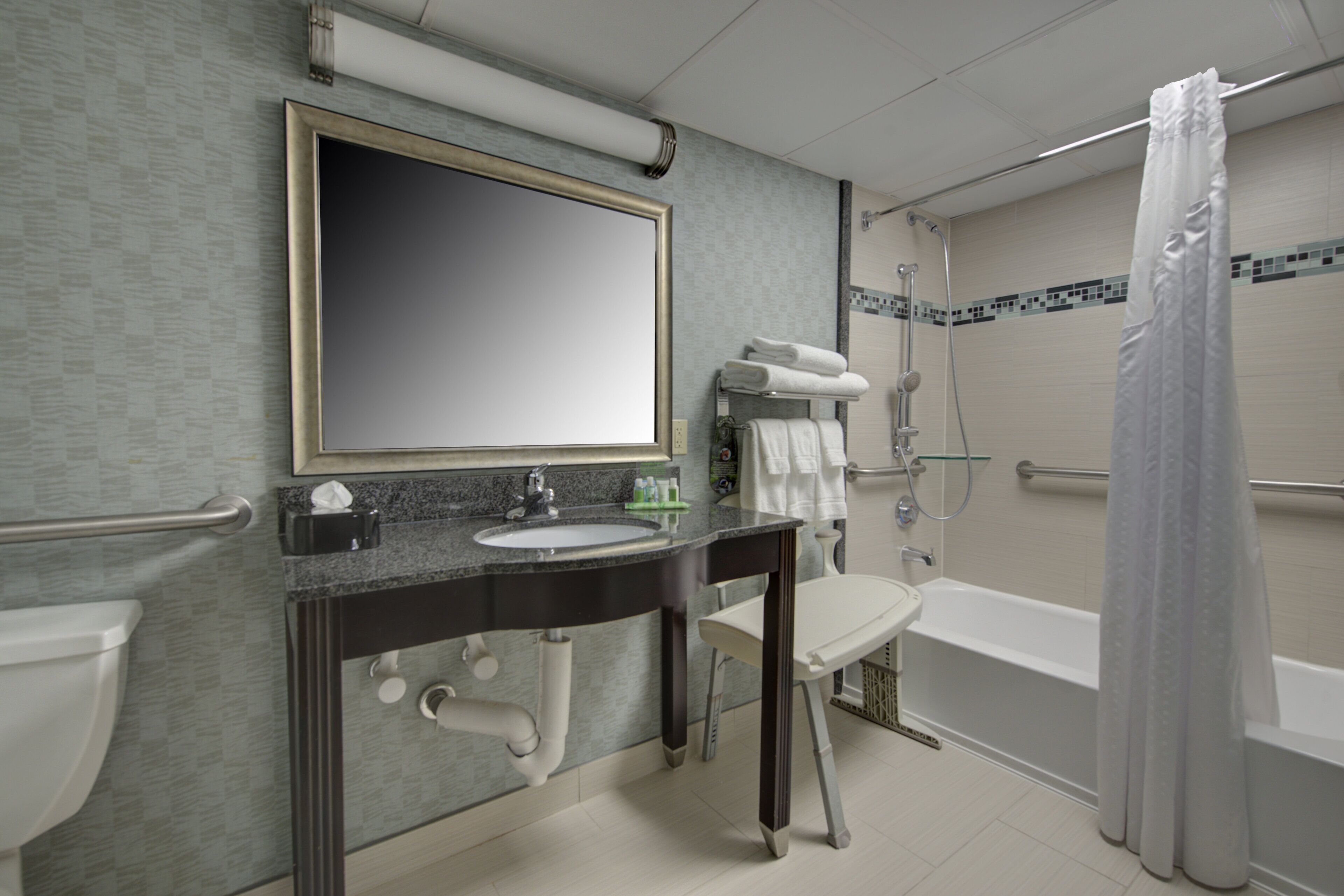 A bathroom with a sink, mirror, towel rack, shower, and toilet.