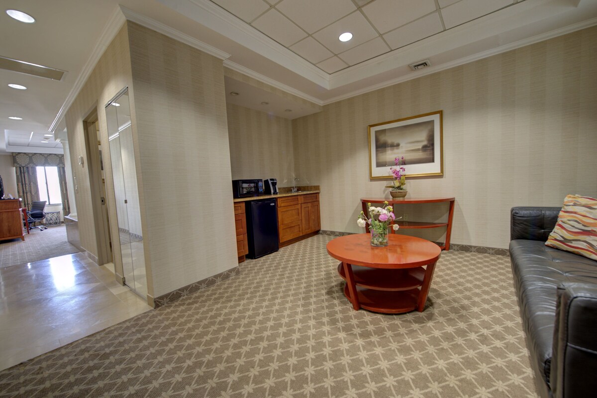 A hotel room with a dining area, a sofa, a coffee machine, and a framed picture on the wall.