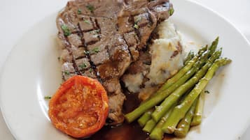 Un plato con un bistec a la parrilla, puré de papas, espárragos y una rodaja de tomate.