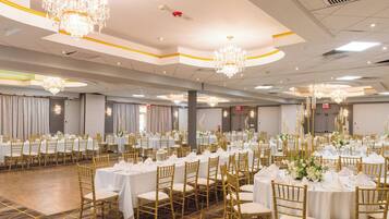 Un salón de banquetes con mesas redondas, sillas doradas, manteles blancos y candelabros.