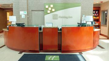 Una recepción con mostrador de check-in, un letrero de Holiday Inn y un tapete negro con el texto 'Plainview A JGroup Hotel'.