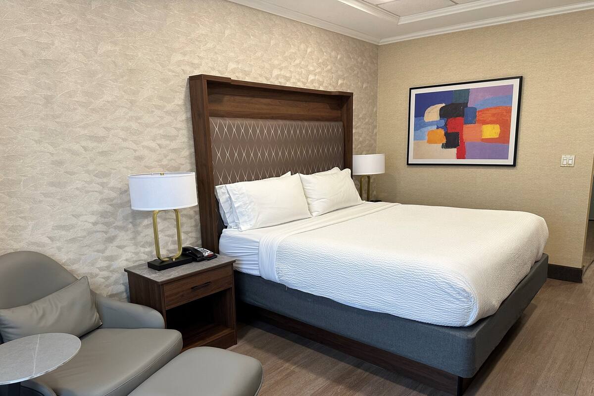 Habitació d'hotel amb un llit gran, un escriptori amb una làmpada, una cadira i una taula petita.