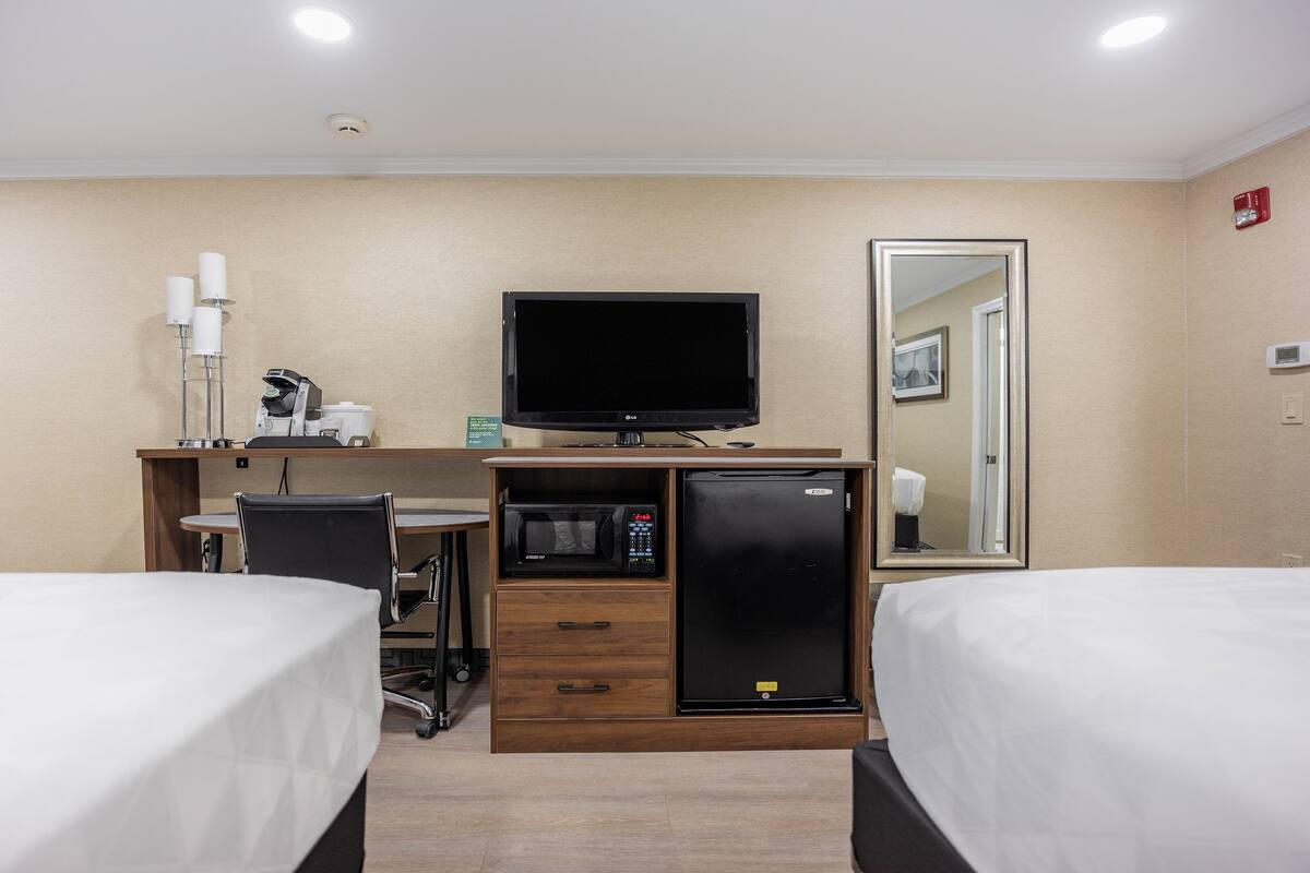 Una habitació d'hotel amb dues lliteres, un escriptori amb un ordinador, un microones i un frigorífic.