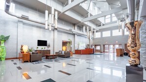 A spacious lobby with a high ceiling, a reception desk, seating area, and a large decorative sculpture. - Holiday Inn Plainview-Long Island by IHG (Plainview)