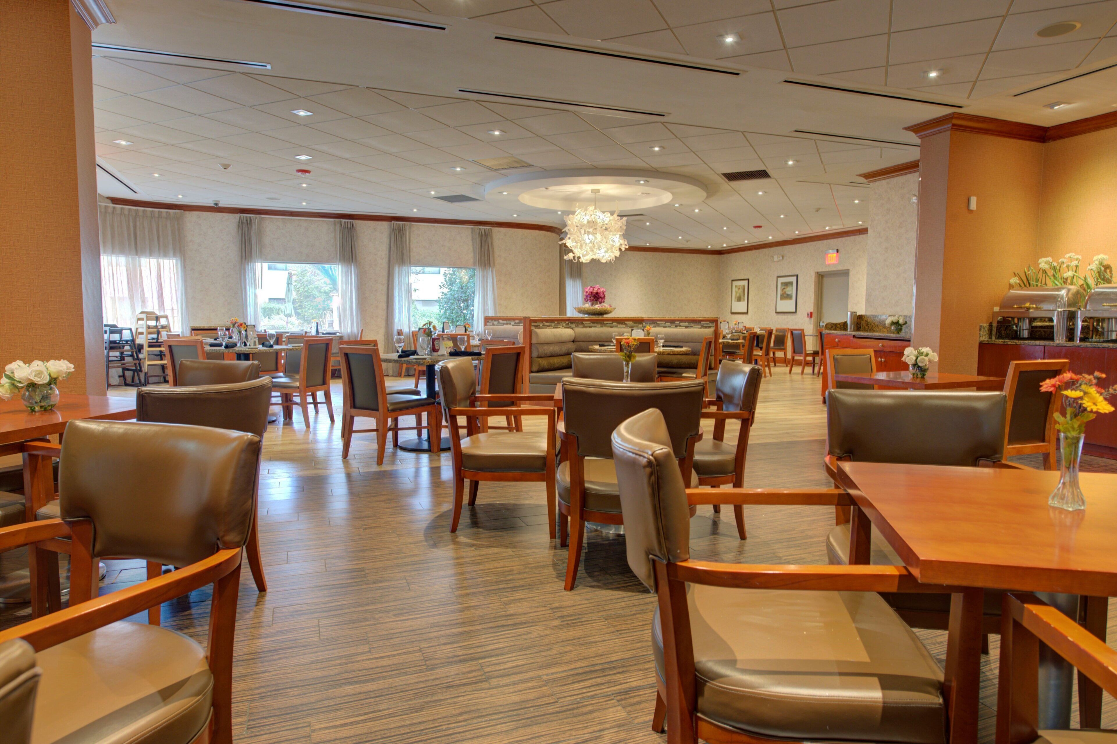 A hotel lobby with multiple seating areas, including tables and booths, a central chandelier, and a reception desk.