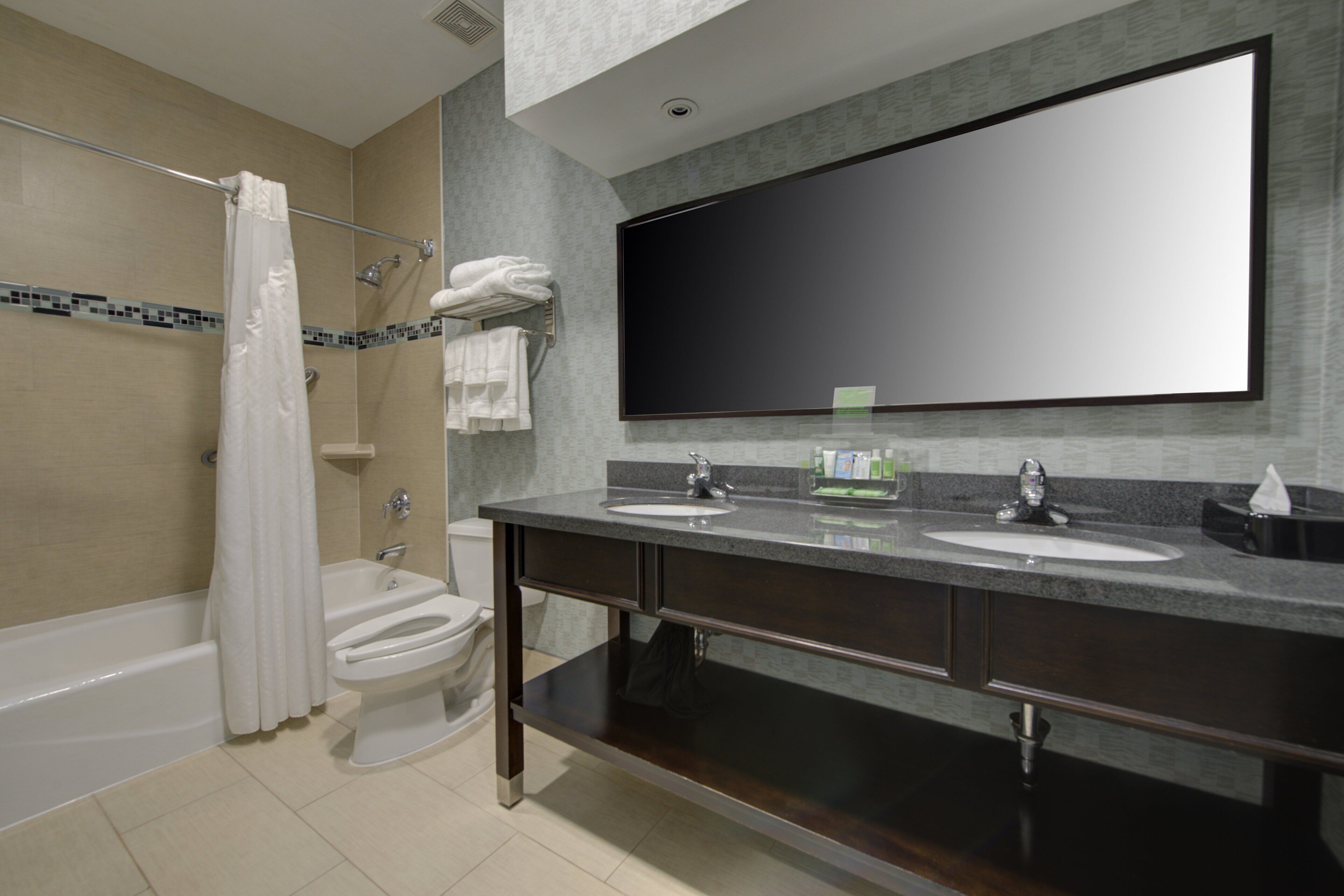 A modern bathroom with a bathtub, two sinks, a toilet, and a large mirror.