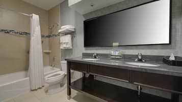 A modern bathroom with a bathtub, two sinks, a toilet, and a large mirror.