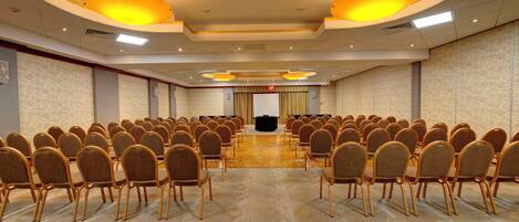 A conference room with rows of chairs facing a stage, equipped with overhead lighting and a podium.