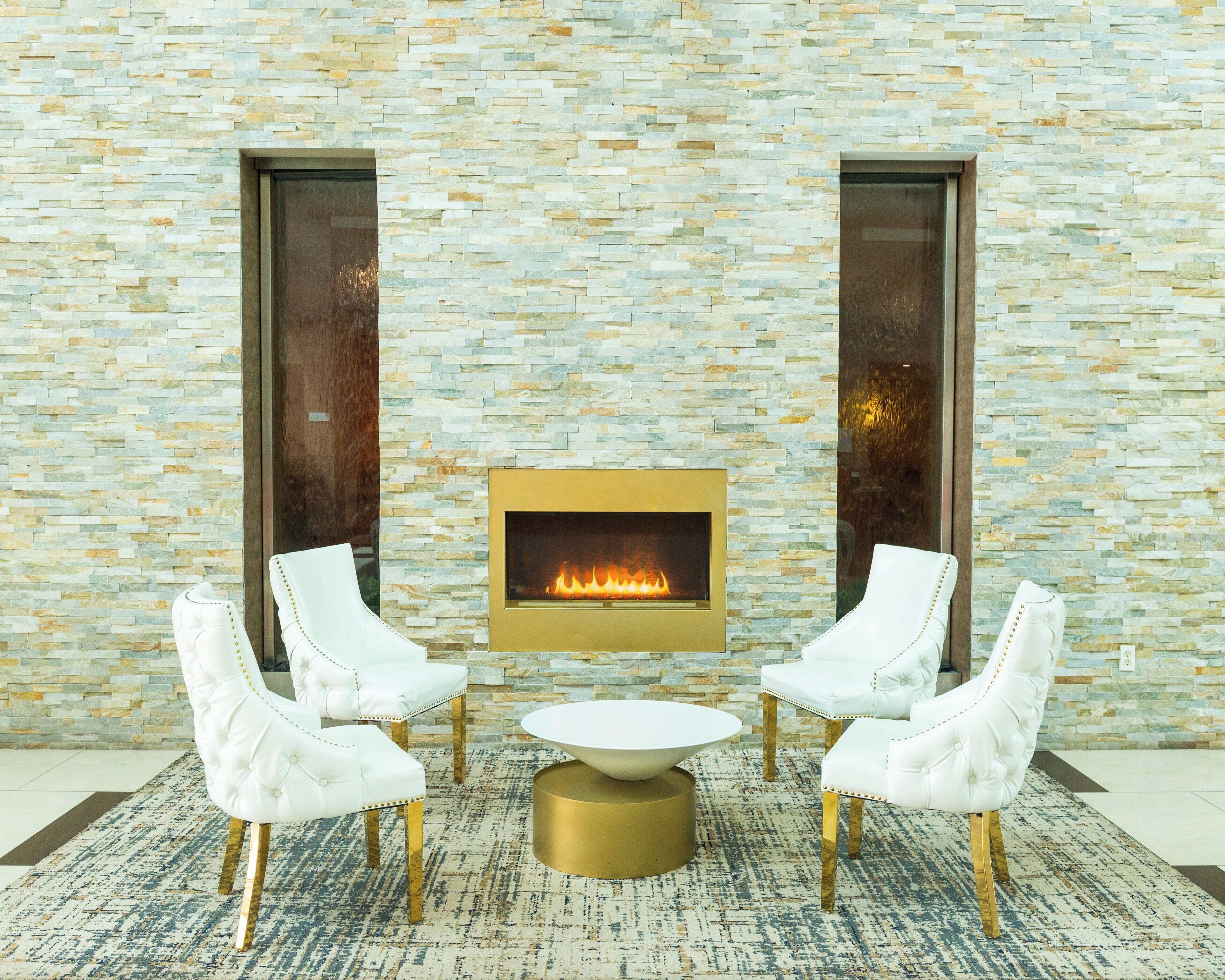 A stone wall with a fireplace, white chairs, and a round table.