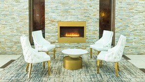 A stone wall with a fireplace, white chairs, and a round table. - Holiday Inn Plainview-Long Island by IHG (Plainview)