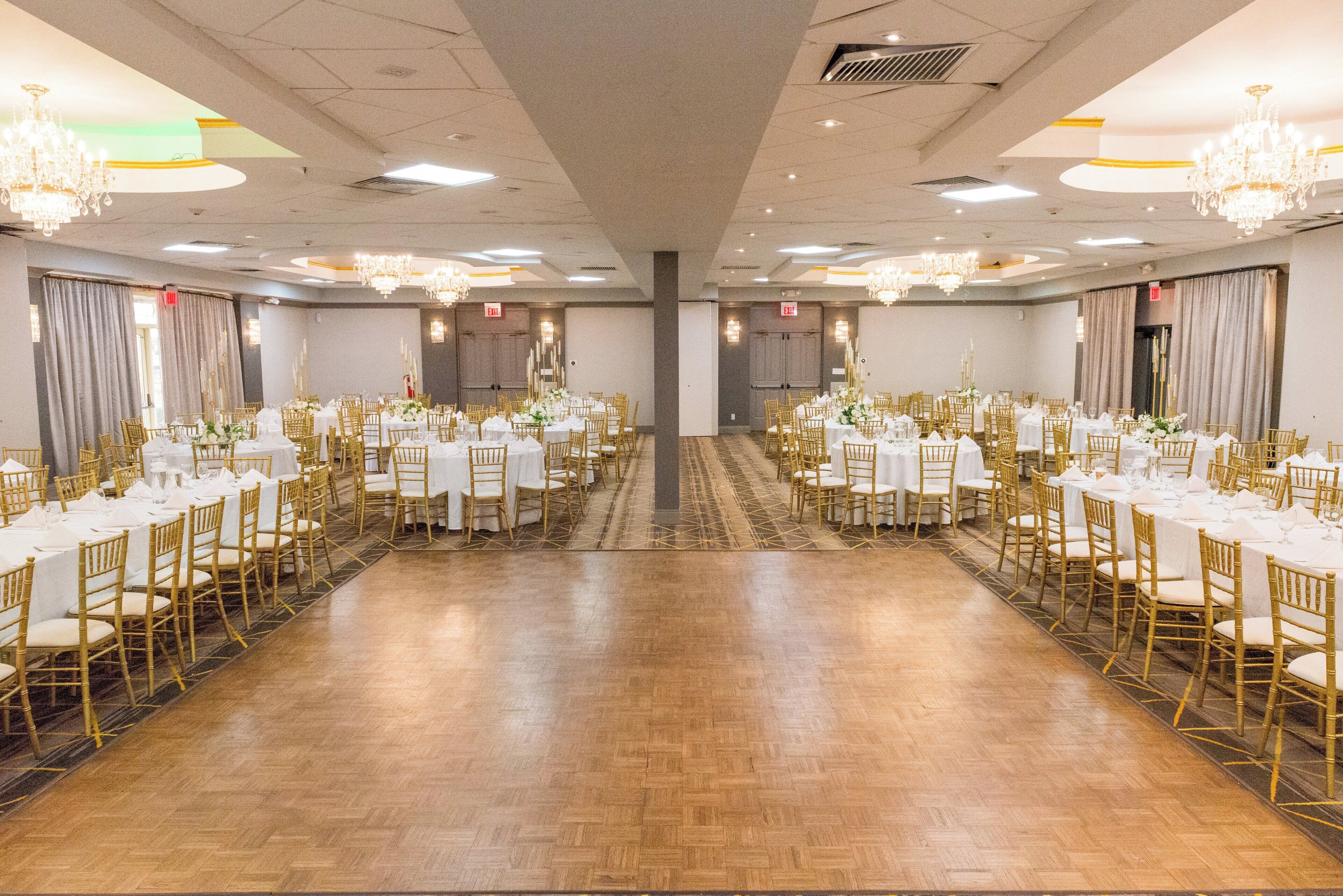 Un salón de banquetes con mesas redondas, sillas doradas, candelabros y piso de madera.