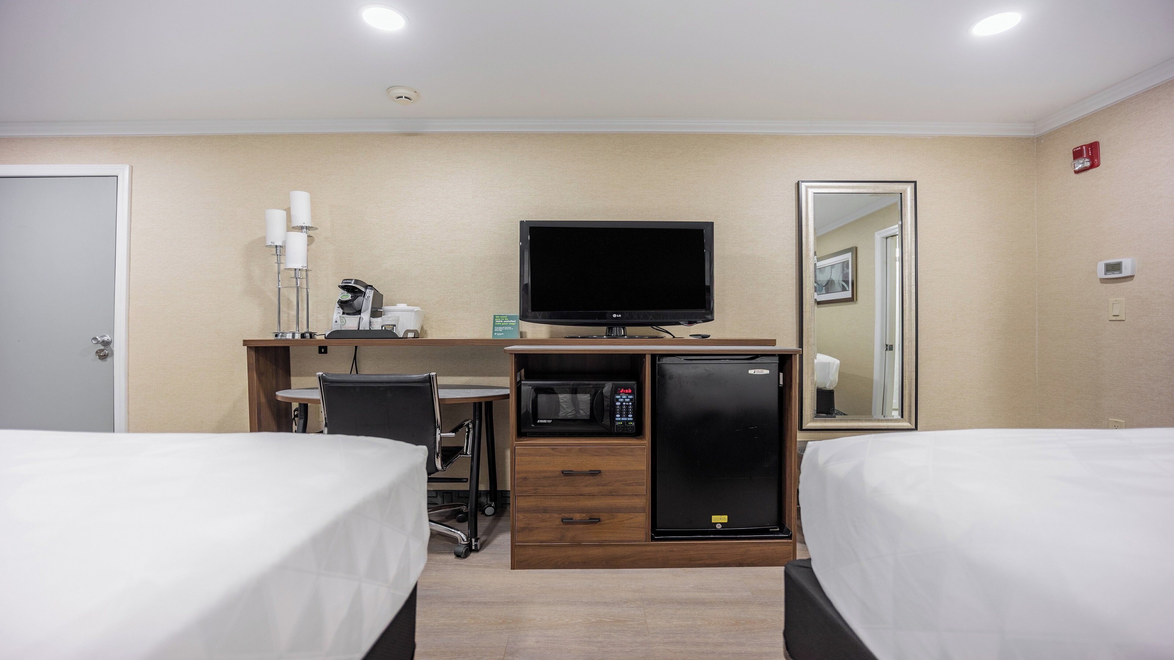 A hotel room with two beds, a desk with a computer, a microwave, and a refrigerator.