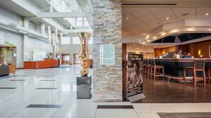 A spacious lobby with a reception desk, a stone pillar with a sign, a bar area, and a large sculpture. - Holiday Inn Plainview-Long Island by IHG (Plainview)